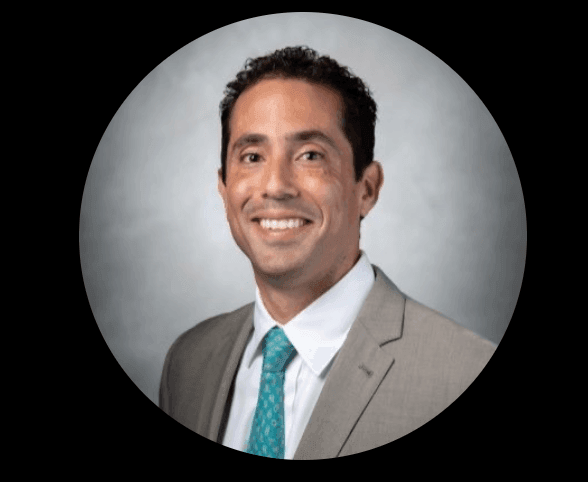 Profile image of a man wearing a gray suit and turquoise tie against a gray background.