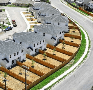 Aerial view of a row of identical white houses with fenced backyards in a suburban neighborhood.